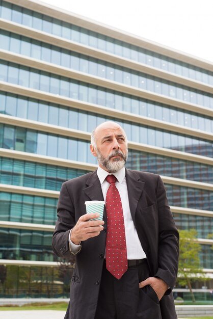 pensive-mature-businessman-holding-paper-cup-street_74855-3604